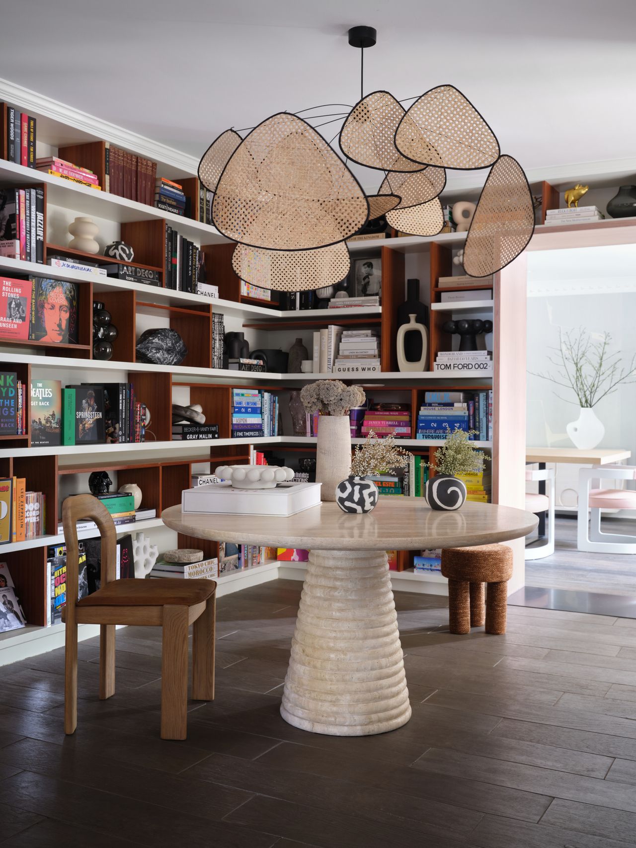 a room with a bookshelf wall, a round table, chairs, and an elegant light fixture