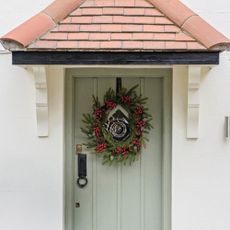 A sage green front door with a berry-encrusted Christmas wreath on it