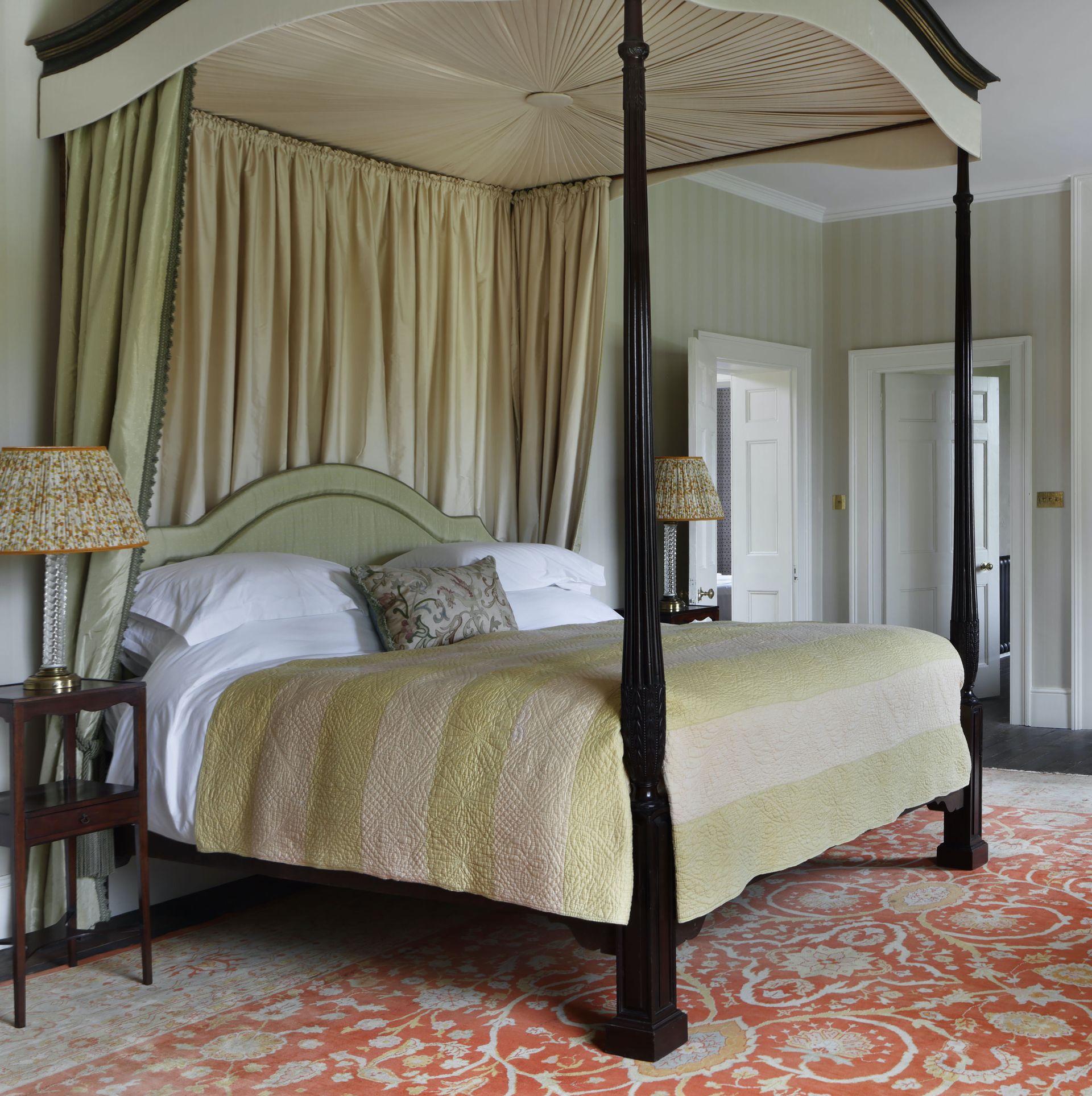 Black, wooden four posted bed, striped green blanket and wallpaper