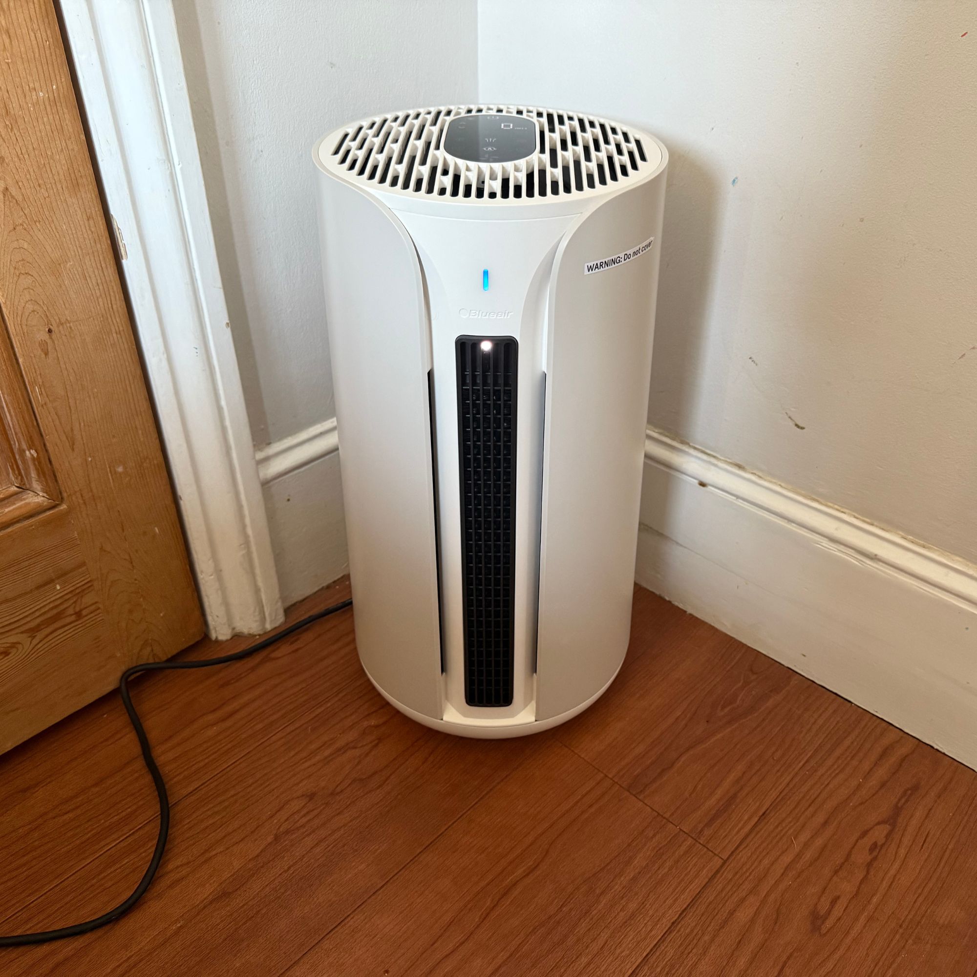 Blueair ComfortPure 3-in-1 T10i Air Purifier sitting on wooden floor in front of a grey wall