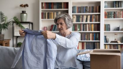 Dissatisfied woman holds up a shirt she has taken out of a box.