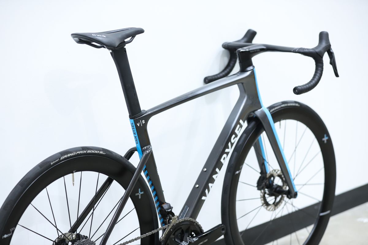 A blue and grey Van Rysel RCR Pro stands against a white wall