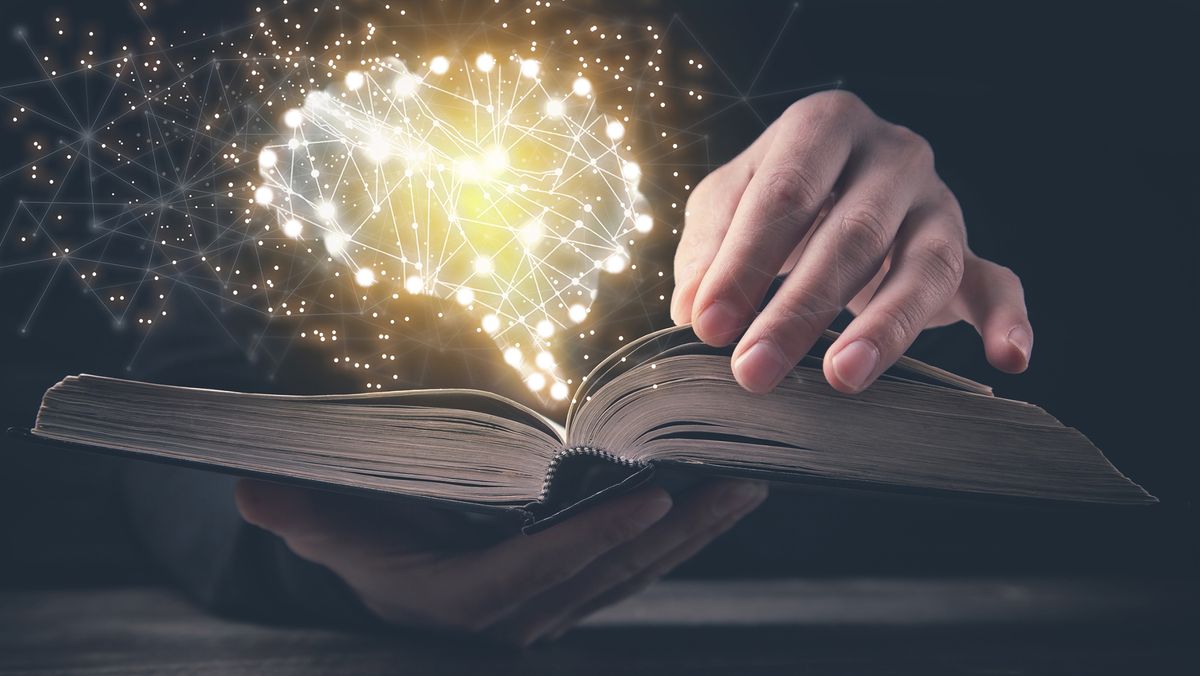 A book open in a person&#039;s hand with a glowing impression of a human brain popping out of it.