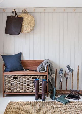 neutral hallway with painted wall panelling with wall hooks and a bench to create a boot room feel