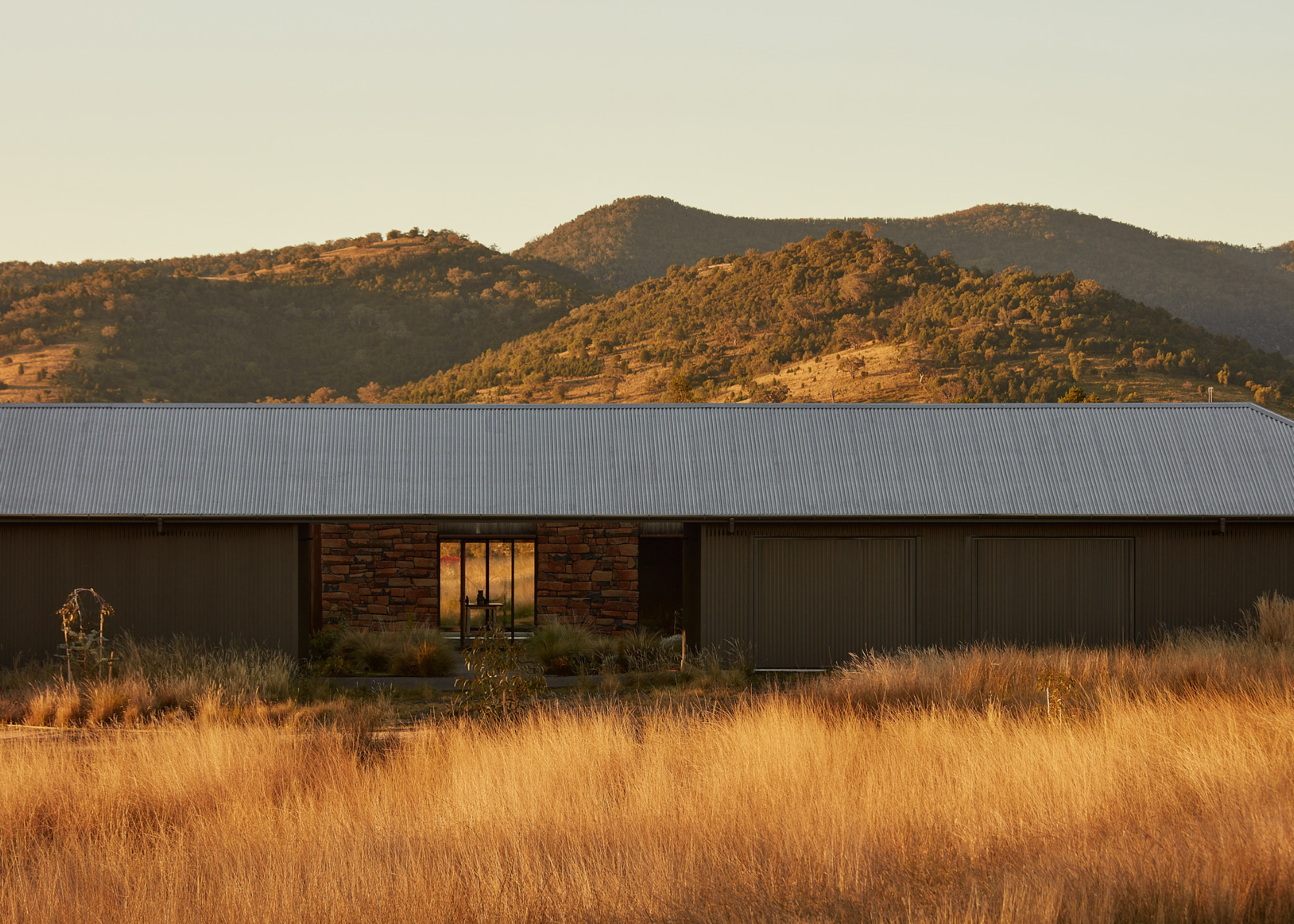 a house set against a mountainous Australian landscape with wild, ornamental grass growing all around it