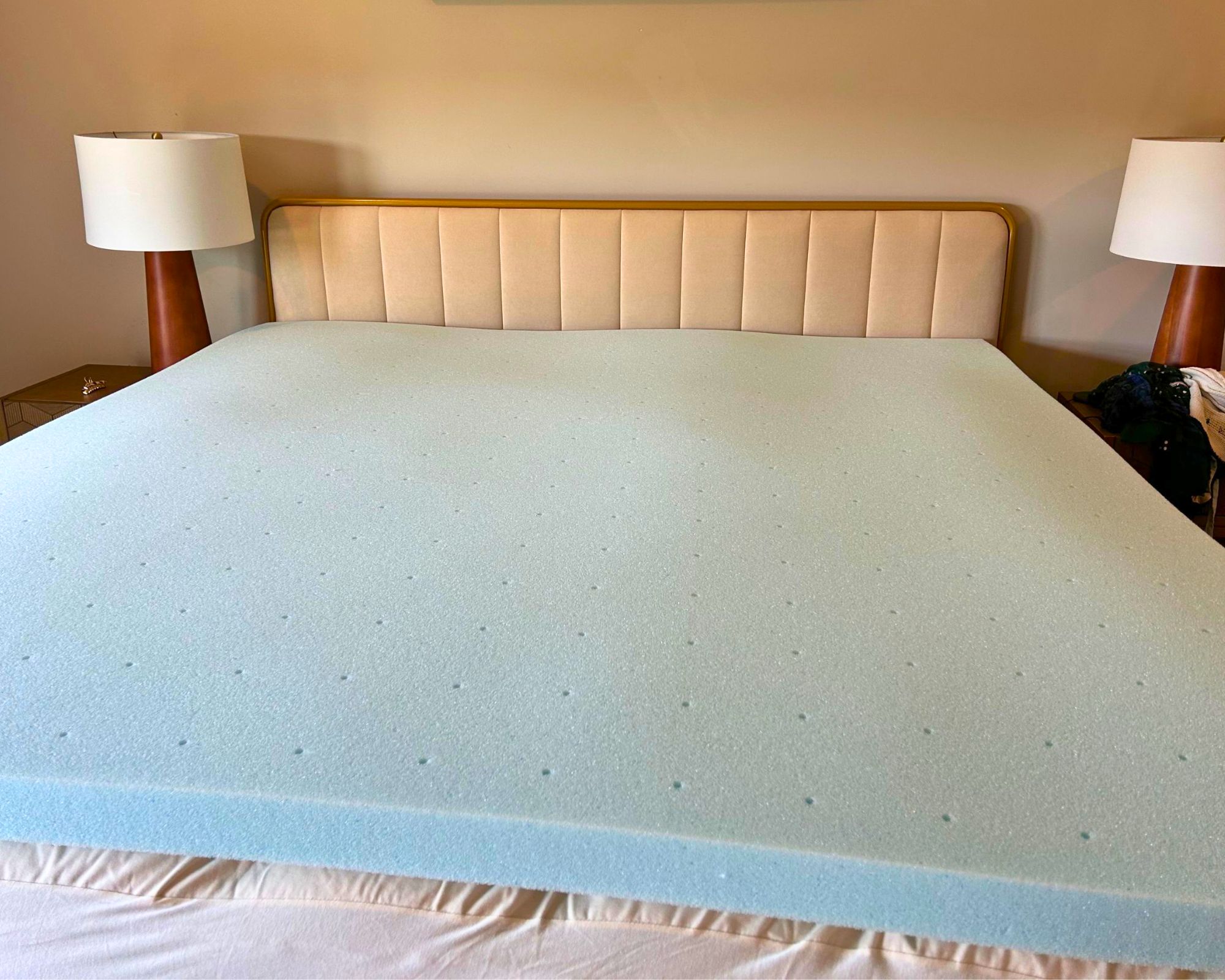 A blue Lucid mattress topper photographed in a white bedroom on a white fluted bed with matching wooden lamps with white shades to either side.