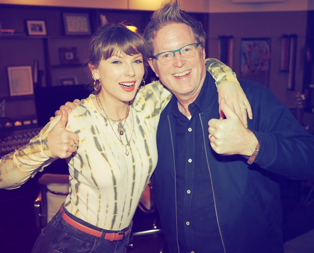 Taylor Swift wearing a tie-dye Agolde bodysuit with black jeans and opal jewelry with brown bangs and a ponytail posing in a recording studio