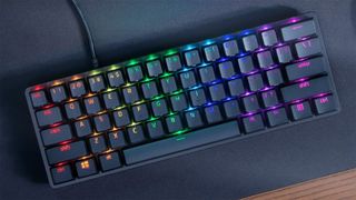 A compact mechanical keyboard with colorful RGB backlighting on each key, set against a dark desk surface, creating a vibrant and modern aesthetic.