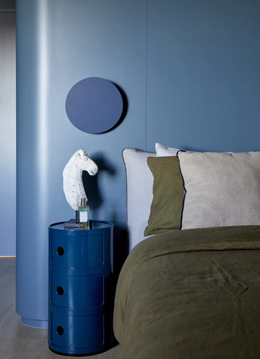 Image of a blue bedroom with a blue side table and a bed that has olive green bedding.