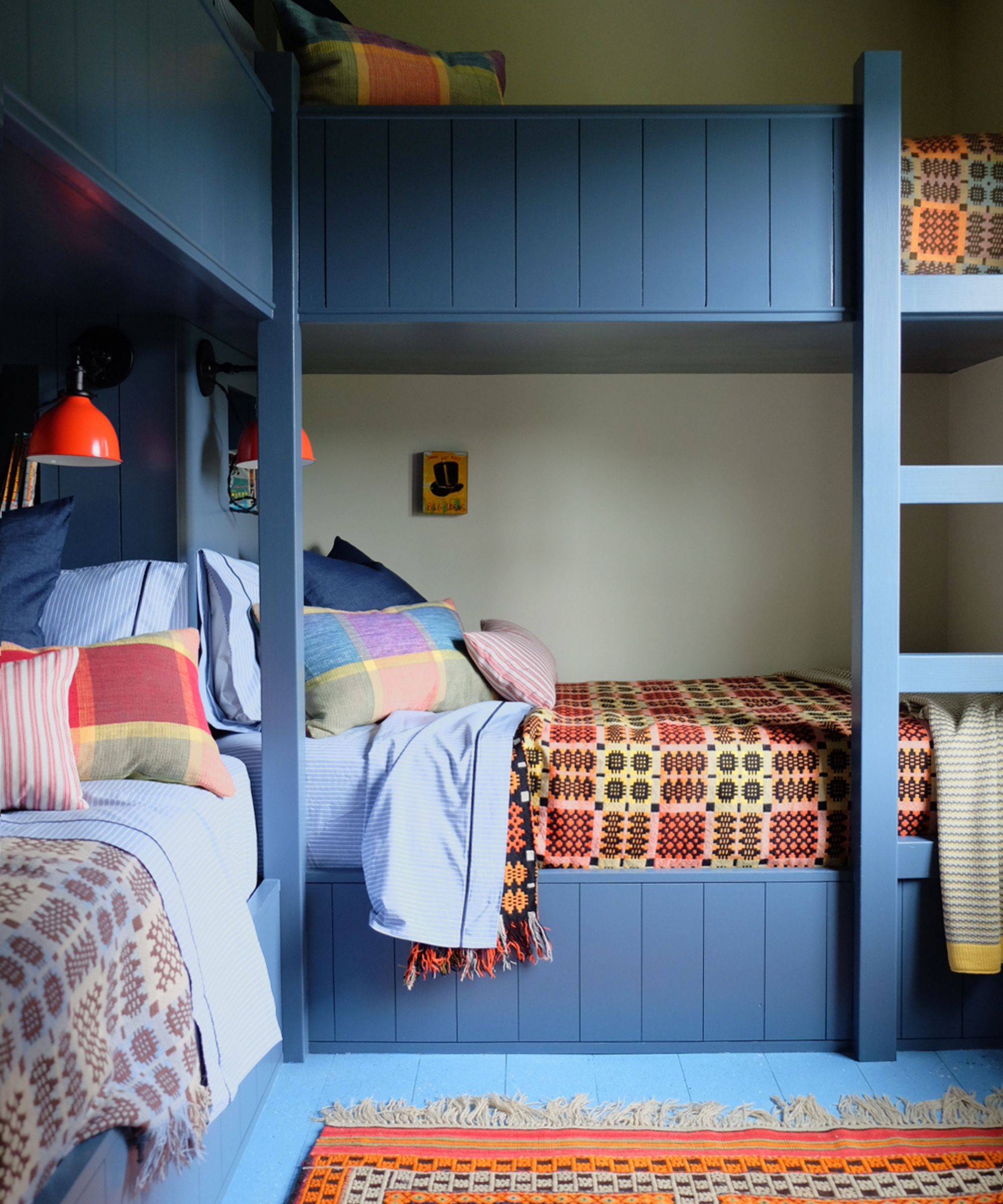 a bunk bedroom in a New England guest cottage with painted dark blue bunks, lighter blue painted floorboards and beds made up with plaid pillows and welsh blankets