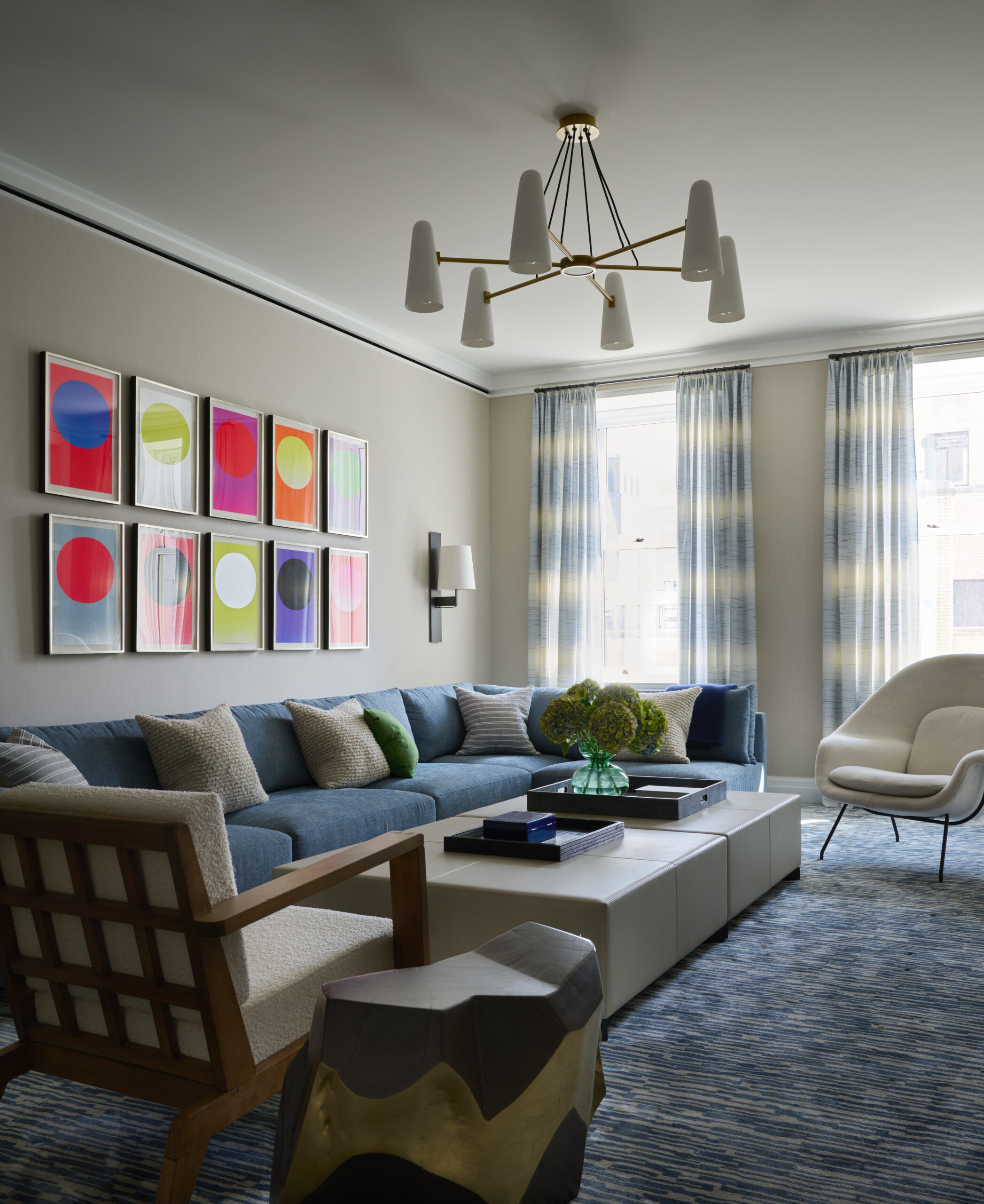 Modern beige living room with bright artwork on the walls and a blue corner sofa and cream armchairs