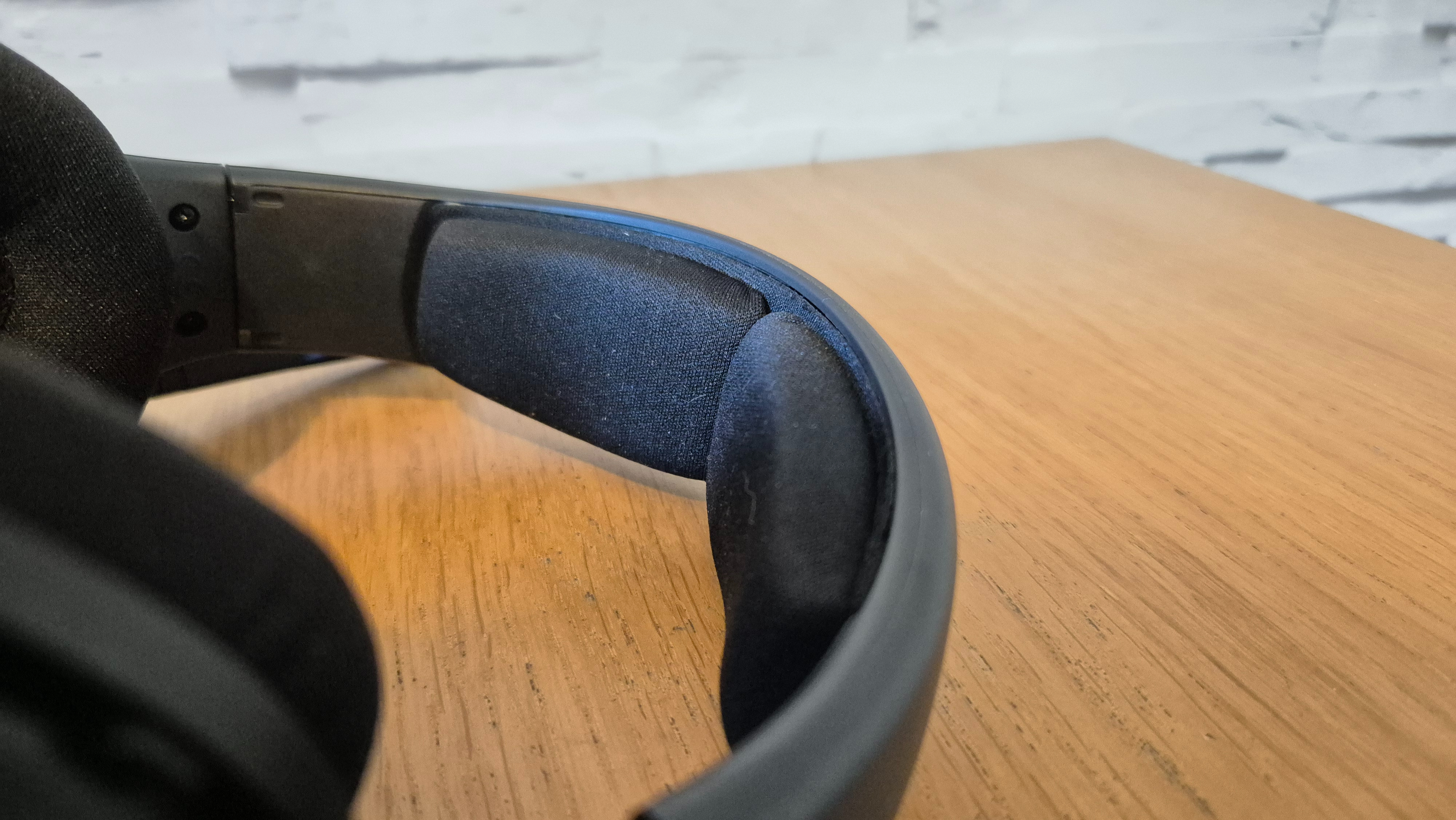 The Drop + Epos PC38X headset on a wooden surface in front of a white brick wall