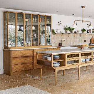 kitchen with terracotta floor tiles, a large reclaimed glass-fronted dresser, a kitchen island with shelving and drawers and a neutral-tiled kitchen splashback