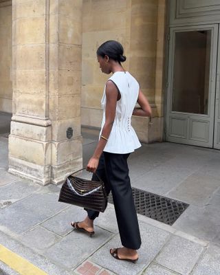 Sylvie Mus wearing a white sleeveless blouse with black cropped pants, a brown bag, and black kitten heel sandals.