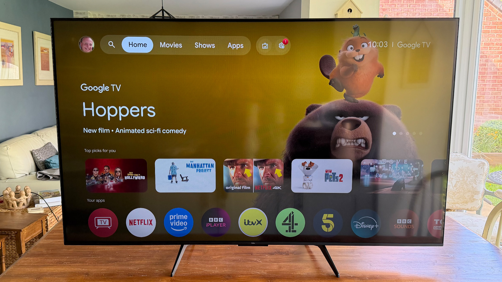 TCL Q6C 65-inch LCD TV on wooden dining table, on screen is Google TV home screen