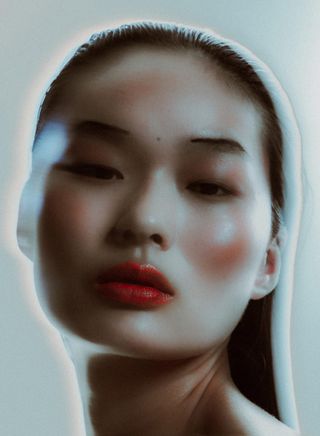 Closeup photo of an Asian woman with slicked back hair wearing bright makeup.