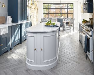 A neptune kitchen with rounded oval kitchen island in white between runs of blue cabinetry with a dining table in the background.