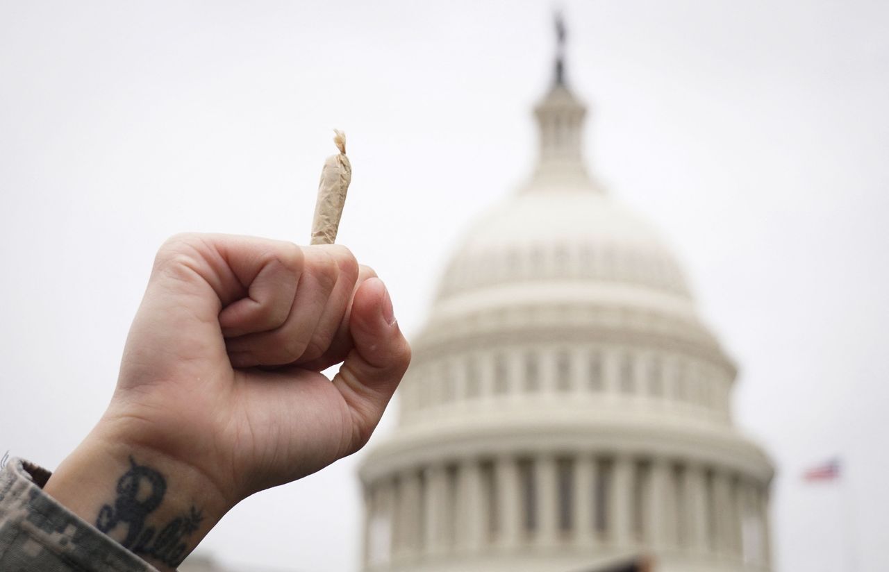 Hand holding joint in front of US Capitol dome