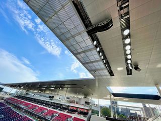 An outdoor stadium adorned with an L-Acoustics sound system hanging from the upper deck.