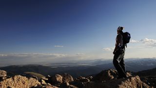 A hiker stands at the top of a high peak in Colorado looking at the view