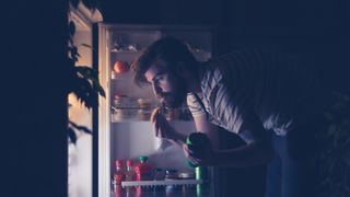 man looking for a snack in his fridge during the night
