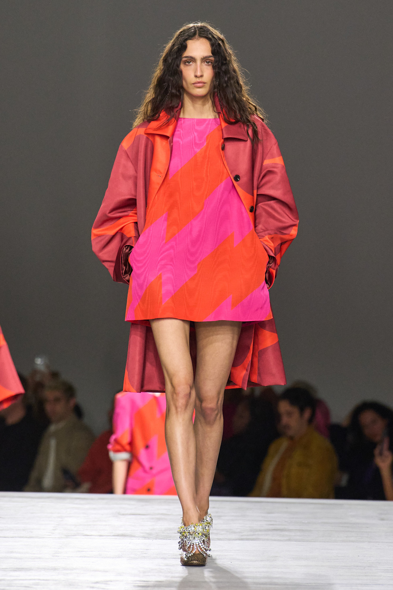 A model at the spring/summer 2026 Dries Van Noten show wearing a striped pink-and-orange dress with a patterned car coat.
