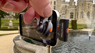 Shot of a hand holding a Lark M2S mic to show off the orange noise reduction button