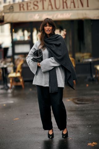 A woman wearing a fall outfit idea of a gray shawl, gray sweater, black pants, black shoes at Paris Fashion Week