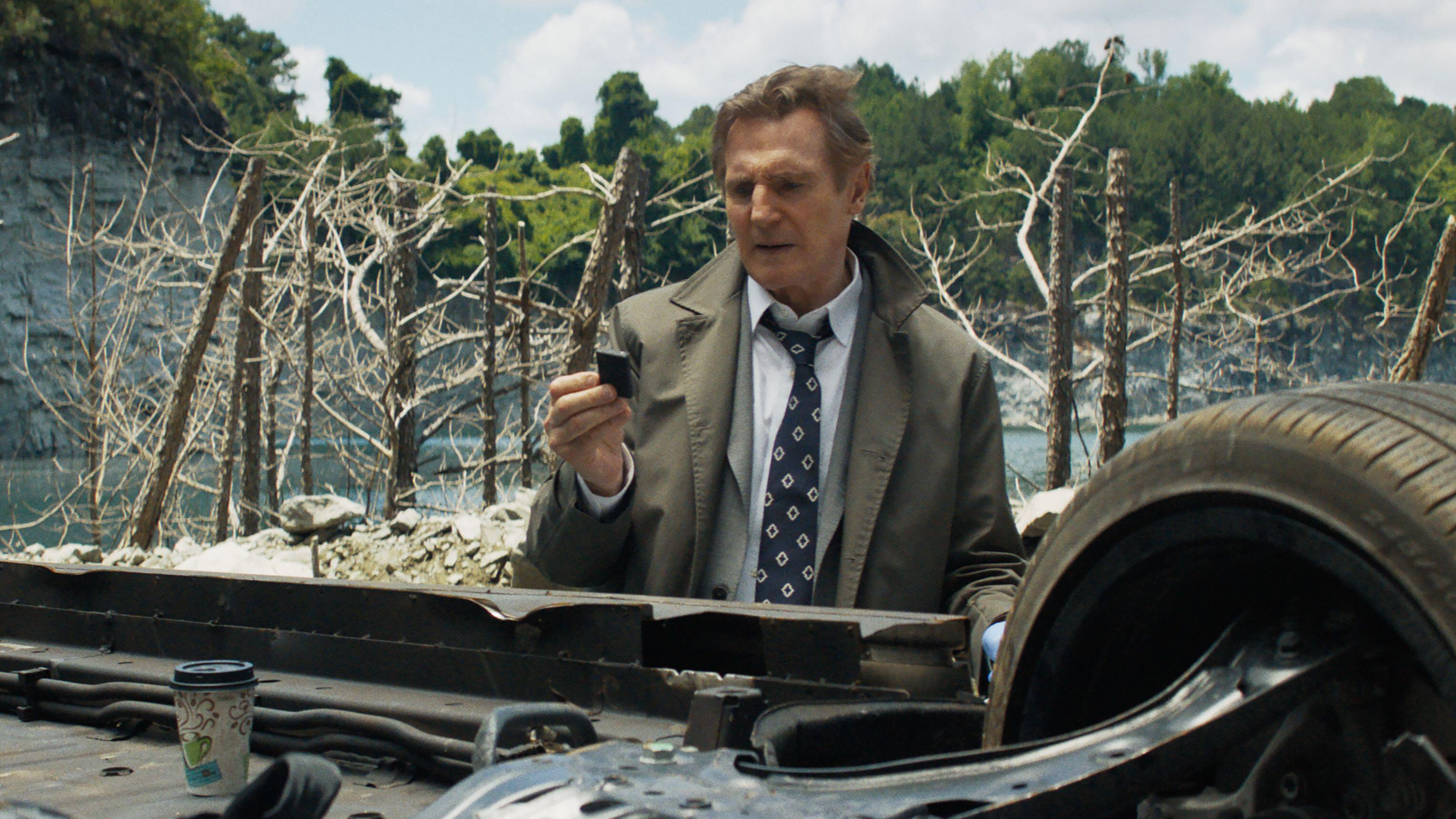 Frank Drebin Jr (Liam Neeson) inspects a car wreckage in a scene from "The Naked Gun" (2025)