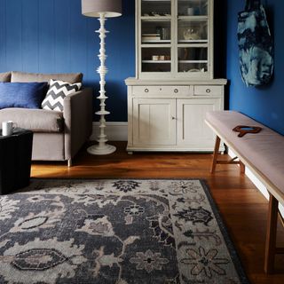 living are with blue wall and wooden floor and rug and grey sofa with cushions and bench and cupboard