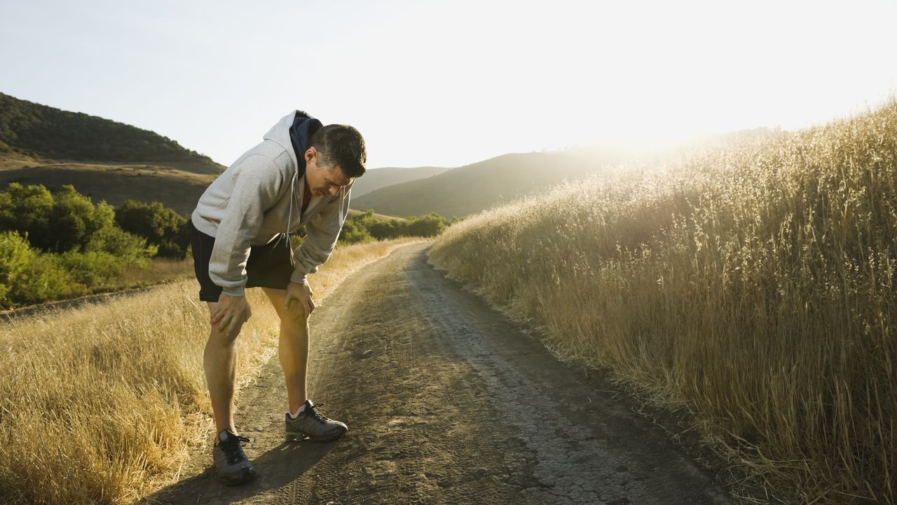 A man who&#039;s been running stops to take a breather one a path through a field.