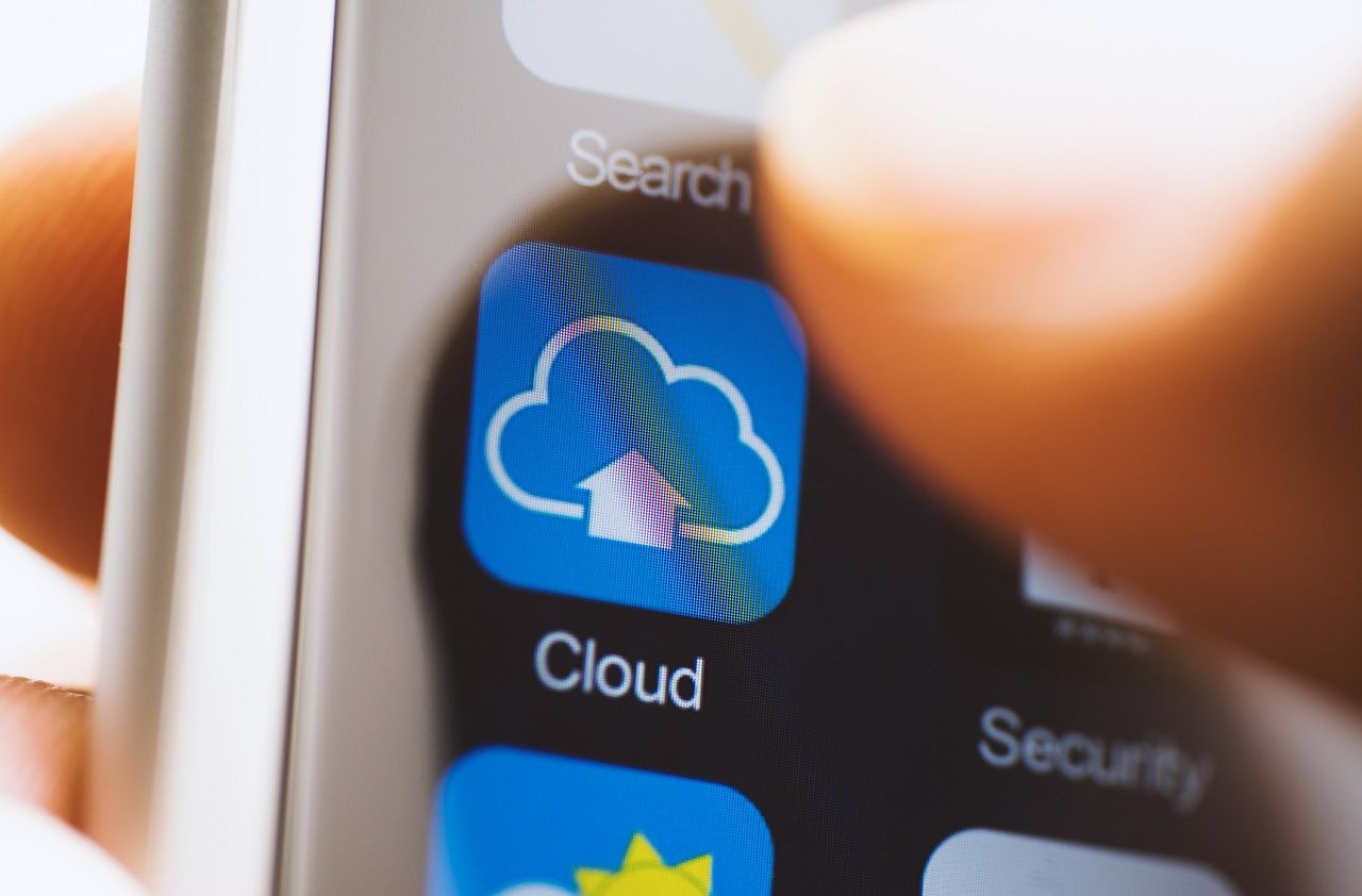 Hand holding phone, finger touching cloud computing app icon on screen