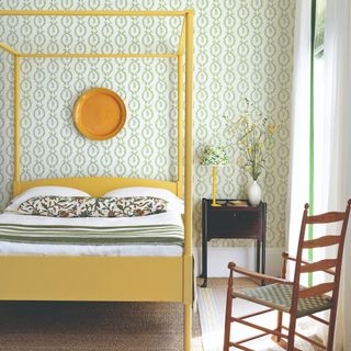 A bedroom with a yellow canopy bed and a botanical wallpaper in green and cream on the walls