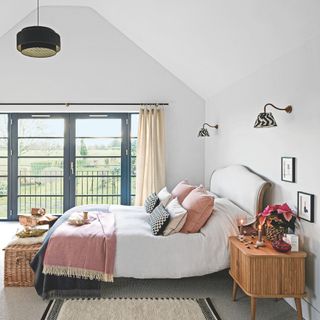 White bedroom with vaulted ceilings and large windows and doors looking out onto the gsarden, with white bedding