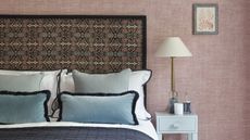 A bedroom with pink walls, a patterned headboard, and throw pillows with fringing