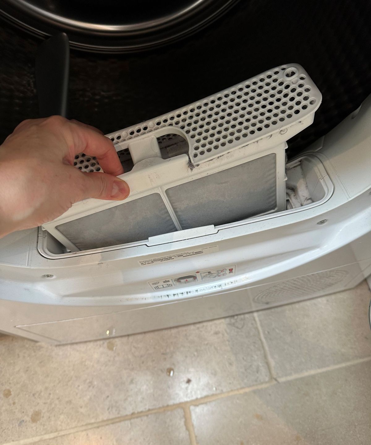 A hand pulling the filter out of the tumble dryer