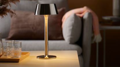 Chrome IKEA portable indoor / outdoor lamp styled atop of a wooden coffee table alongside a tray of crystal-cut glasses