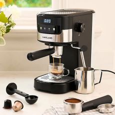 Black coffee machine with portafilter pulling a shot of expresso and a steam wand in a milk jug