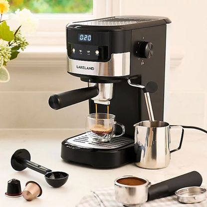 Black coffee machine with portafilter pulling a shot of expresso and a steam wand in a milk jug