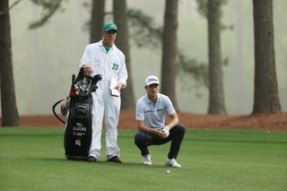 Will Zalatoris crouches next to his golf bag with his caddie stood next to him