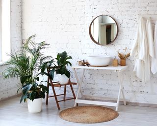 Bathroom interior with big round mirror, table and plants near brick wall