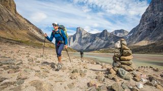 two hikers passing a cairn with the mountains behind them