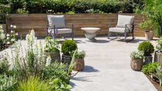 patio design with garden furniture, potted plants and flowerbeds with fence in background