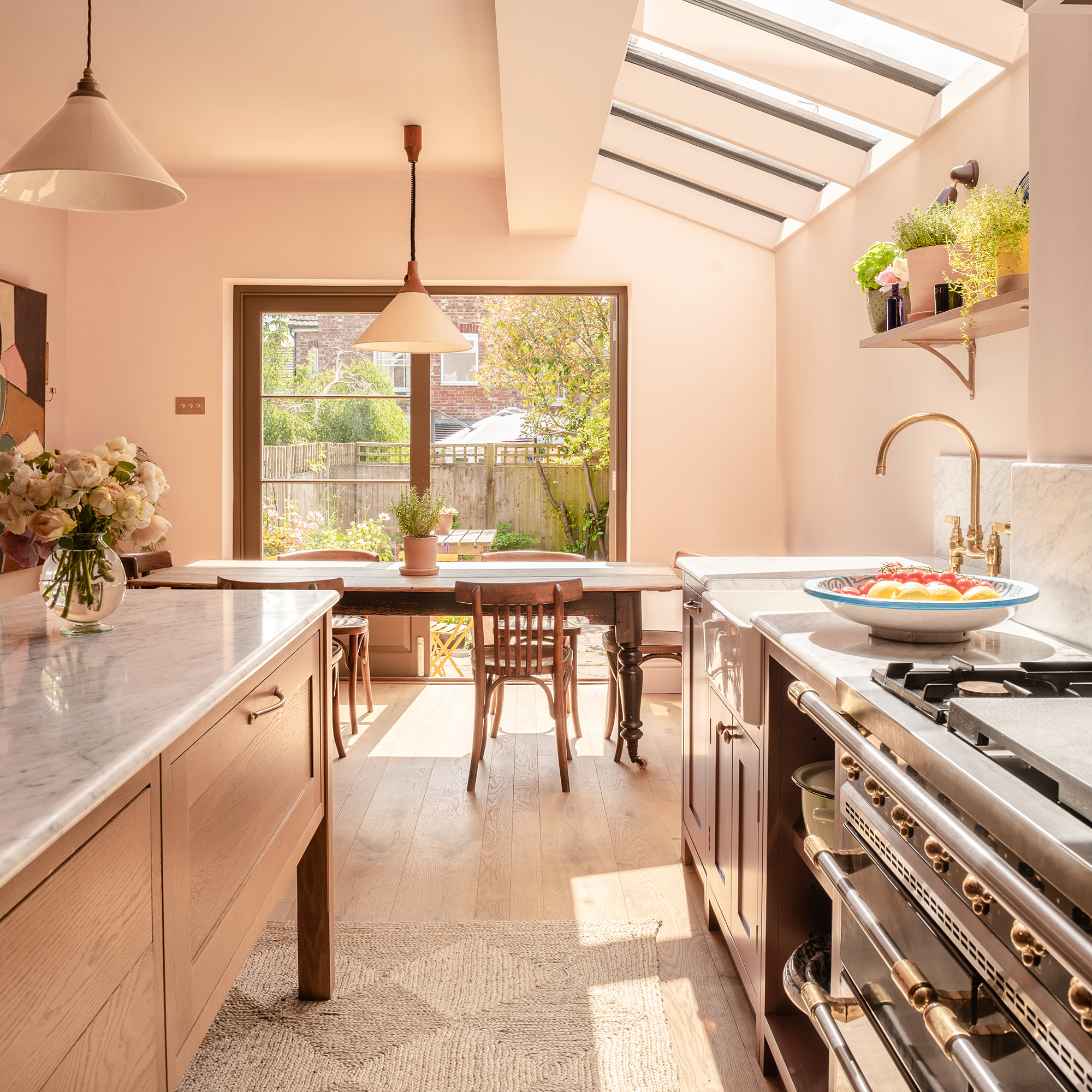 small kitchen with side extension looking towards patio doors and dining table with table and chairs, pink walls and purple cabinetry with wooden freestanding kitchen island and diamond patterned jute rug