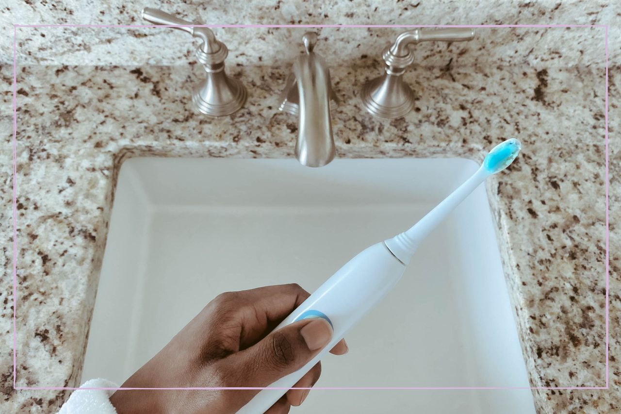 a women&#039;s hand holding an electric toothbrush over a sink