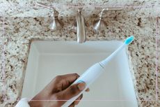 a women's hand holding an electric toothbrush over a sink