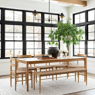 A wooden dining table with chairs in a room with large, black-framed windows.