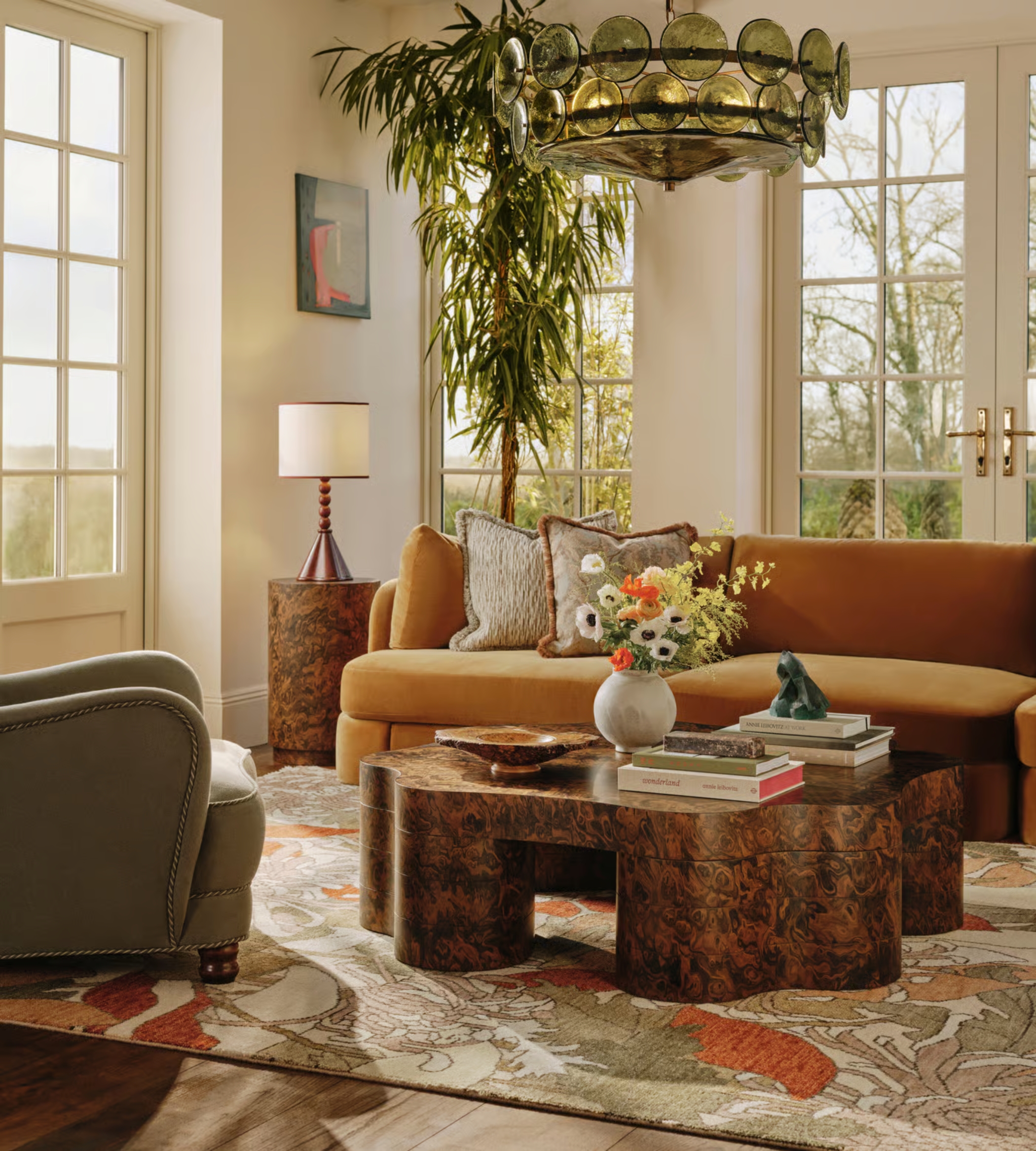 a living room with a burled wood curvy coffee table, patterned rug, and a glass chandelier