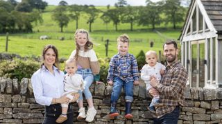 Liz and Kelvin Fletcher stands in front of a wall and fields with their four children Marnie, Milo, Maximus and Mateusz in Fletcher's Family Farm
