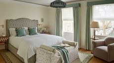 neutral bedroom with wooden floor, a patterned rug, upholstered wavy headboard and green accents with cushions and curtains